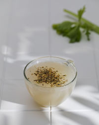 Healthy bone broth with spices in a mug on a white tile with a shadow pattern.