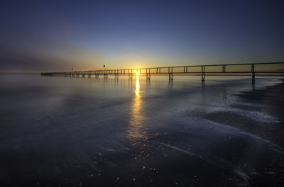 Pier over sea against clear sky during sunset