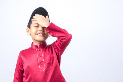 Cute boy wearing maroon traditional clothing standing against white background