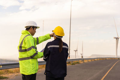 Rear view of engineer examining windmill through digital tablet