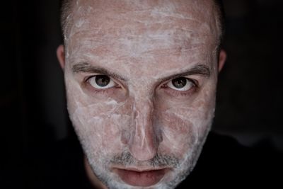 Close-up portrait of man with soap on face against black background