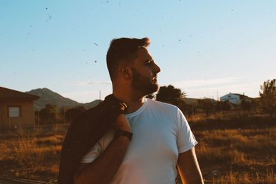 Side view of young man looking away against sky