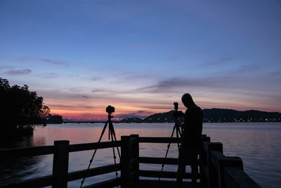 Silhouette man photographing sea against sky during sunset