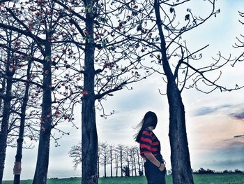 Rear view of woman standing by tree against sky