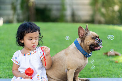 Cute girl blowing bubbles while sitting by dog