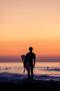Silhouette man standing on beach against clear sky during sunset