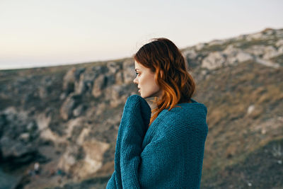 Side view of young woman standing on rock against sky