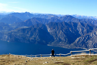 Rear view of man standing on mountain by lake against sky