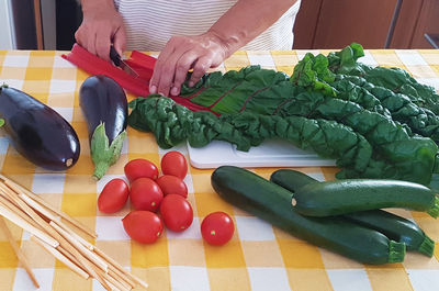 Midsection of woman cutting vegetable at table in kitchen