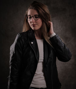 Portrait of young woman standing against black background