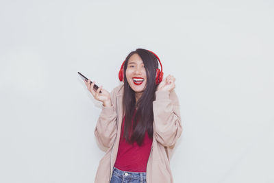 Portrait of young woman using phone while standing against white background