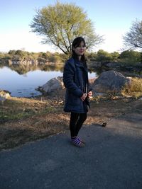 Full length portrait of young woman standing on road against lake