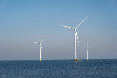 Wind turbines in sea against clear sky
