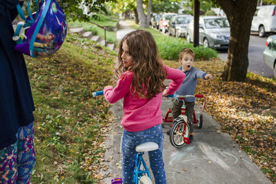 Midsection of mother holding helmet while children riding bicycles on footpath during autumn