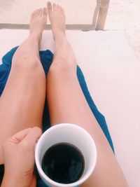 Close-up of barefoot woman holding mug with coffee