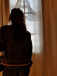 Rear view of woman looking through window at home