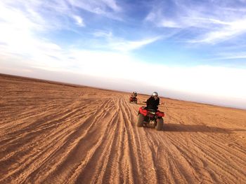 Rear view of people riding quadbikes on desert