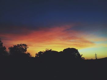 Silhouette trees against dramatic sky during sunset