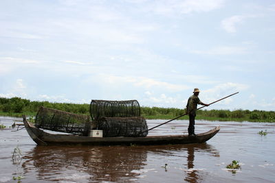 Fisherman oaring boat in lake against sky