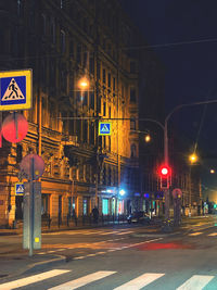 Illuminated road by buildings in city at night