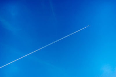 Low angle view of vapor trails in blue sky