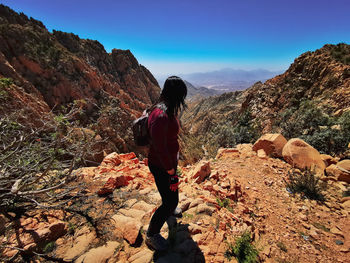 Side view of mid adult woman with backpack standing on mountain against blue sky during sunny day