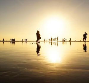 Reflection of silhouette people on beach against clear sky during sunset