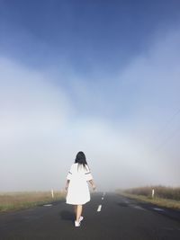 Rear view of woman walking on country road against sky