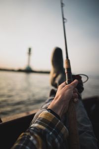 Close-up of man holding fishing rod in boat on sea