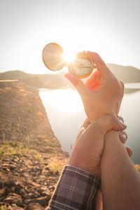 Cropped hands of couple holding navigational compass by lake