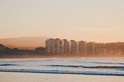 Buildings by sea against sky during sunset