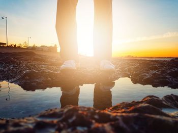 Low section of man standing on rock against sky during sunset