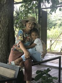 Mother and daughter sitting on tree against plants