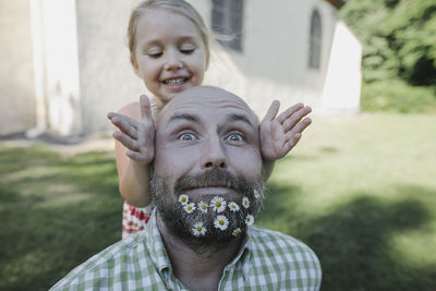 Portrait of mature man with daisies in his beard playing with little daughter in the garden