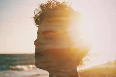 Close-up of woman with closed eyes at beach against sky during sunset