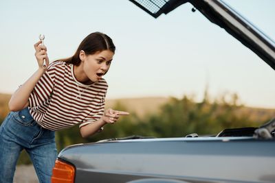 Side view of young woman sitting on car