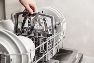 Close-up of hand holding full cutlery basket. loading to, empty out or unloading from dishwasher