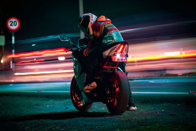 Rear view of man riding motor scooter on road at night
