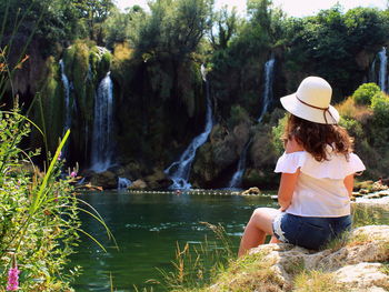 Rear view of woman sitting on rock against trees