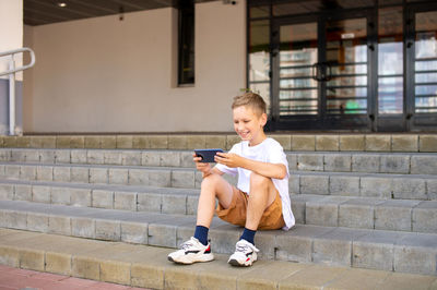 The boy sits on the steps and takes a selfie