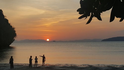 Silhouette people on beach against sky during sunset