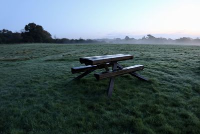 Empty bench on field against clear sky