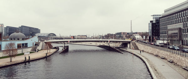 Bridge over river by buildings in city against sky