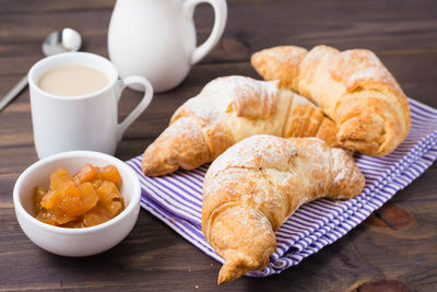 Fresh croissants, a cup of coffee and jam in a bowl on a wooden table. brunch and coffee break