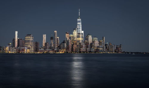 Illuminated city by river against sky at night