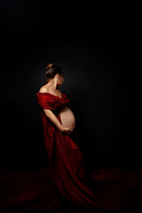 Portrait of young pregnant woman standing against black background