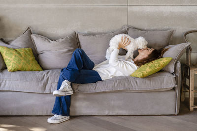 Woman playing with her dog while lying on sofa