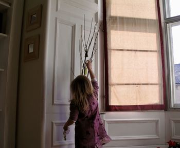 Rear view of woman standing by window at home