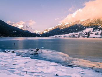 Scenic view of lake by snowcapped mountains against sky during sunset