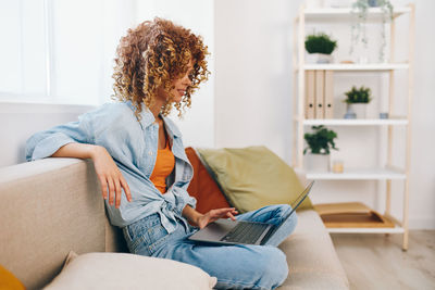 Young woman using digital tablet while sitting on sofa at home